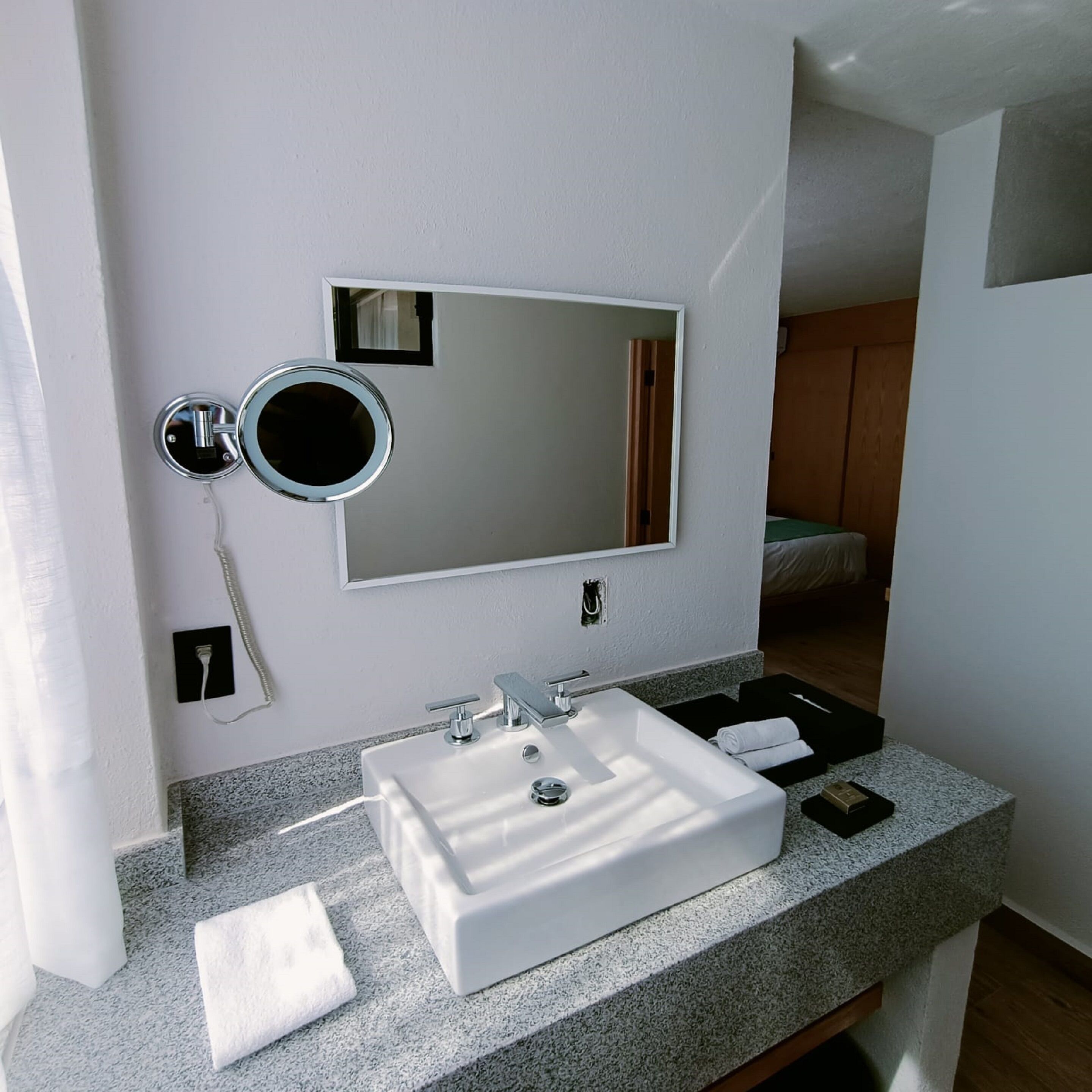 A modern bathroom with a white sink, a mirror, and a small round mirror.