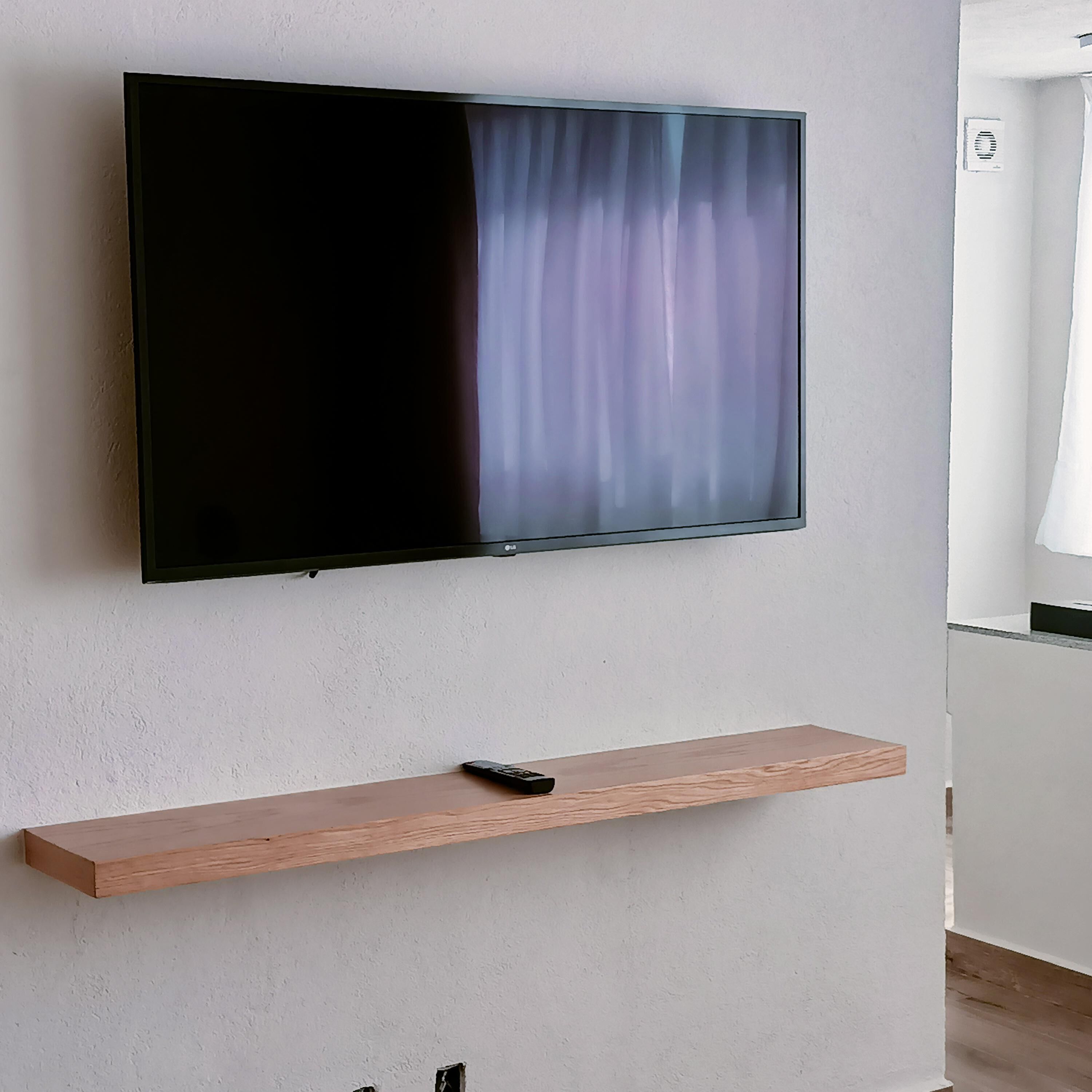 A flat-screen TV mounted on a white wall, with a wooden shelf below it.