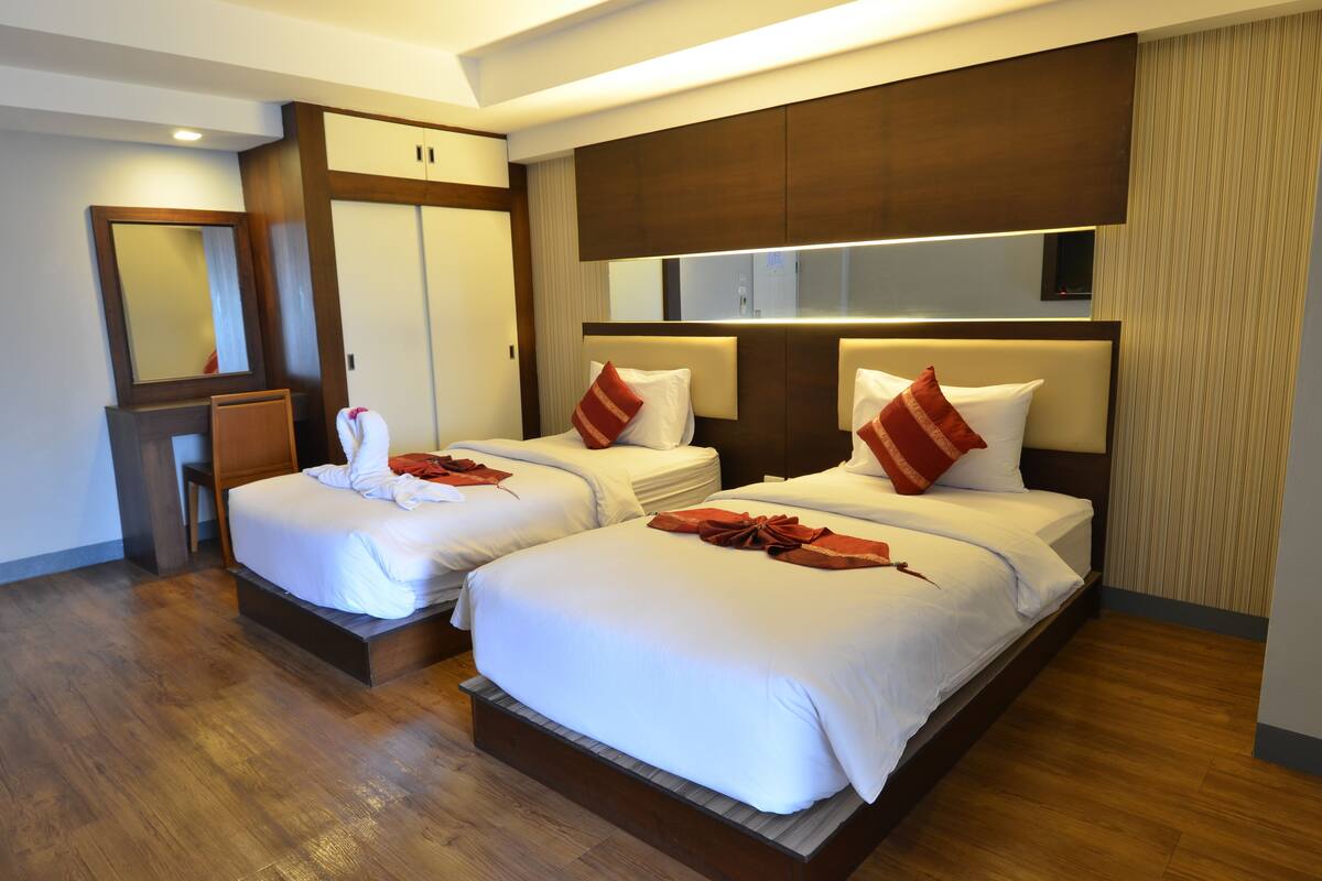 A hotel room with two beds, wooden flooring, a large mirror, and a wardrobe.