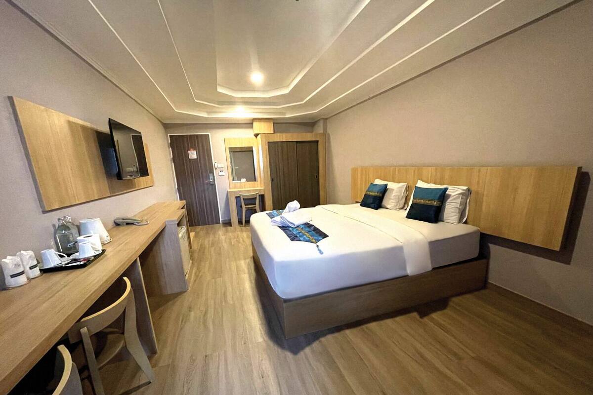 A hotel room with a bed, a desk, a chair, a mirror, and a television.