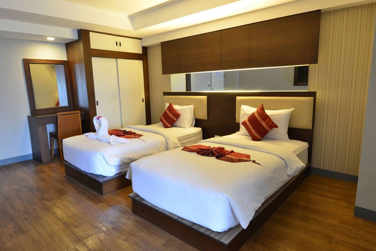 A hotel room with two beds, a desk, a mirror, and a wardrobe.
