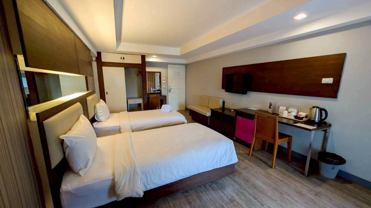 A hotel room with two beds, a desk with a chair, a TV, and a coffee maker.