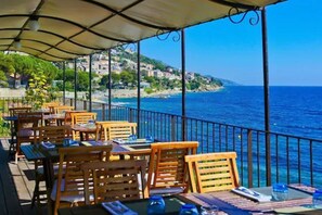 Un espace extérieur aménagé avec des tables et des chaises en bois, offrant une vue sur la côte.