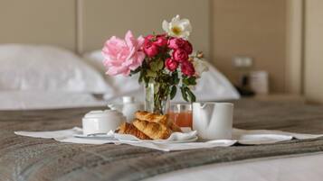 Ein ordentlich hergerichteter Frühstückstisch mit Croissants, einer Blumenvase und einem Saftkännchen auf einem Bett.