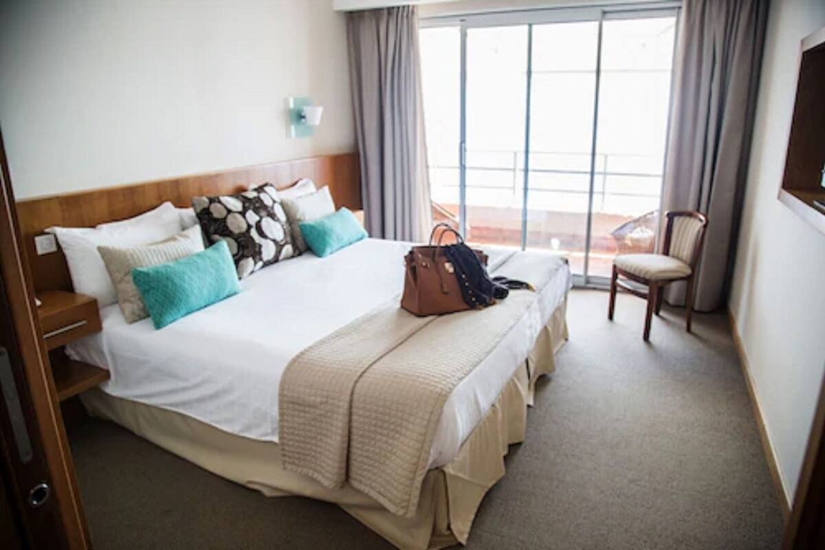 A hotel room with a large bed, a chair, a suitcase, and a view of the outdoors.