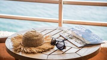 A round wooden table with a straw hat, sunglasses, and a magazine on a balcony overlooking a body of water.