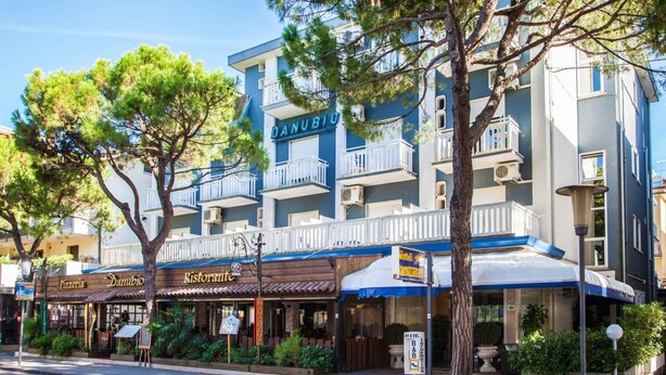 Un hotel con fachada azul, balcones y un restaurante llamado "Danubio Ristorante" en la planta baja.