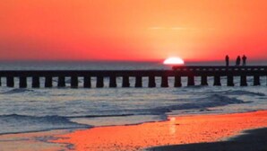 Un atardecer sobre una playa con un muelle y gente de pie al final.