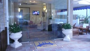 Entrada de hotel con puerta de cristal, felpudo y plantas en macetas.