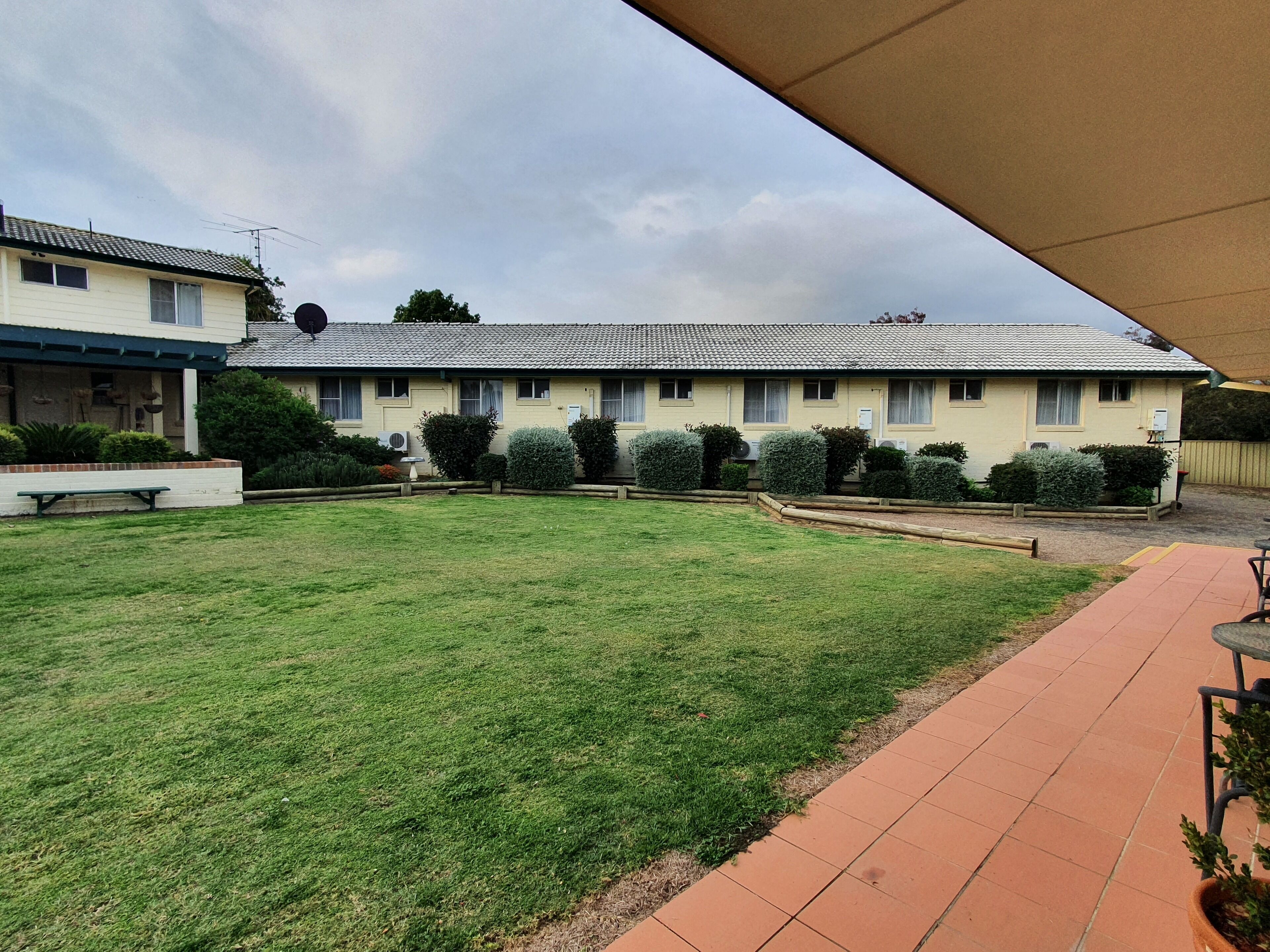 Um edifício de dois andares com telhado plano, entrada com calçamento e gramado bem cuidado.