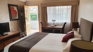 A hotel room with a bed, a desk, a chair, a television, and a window with curtains.