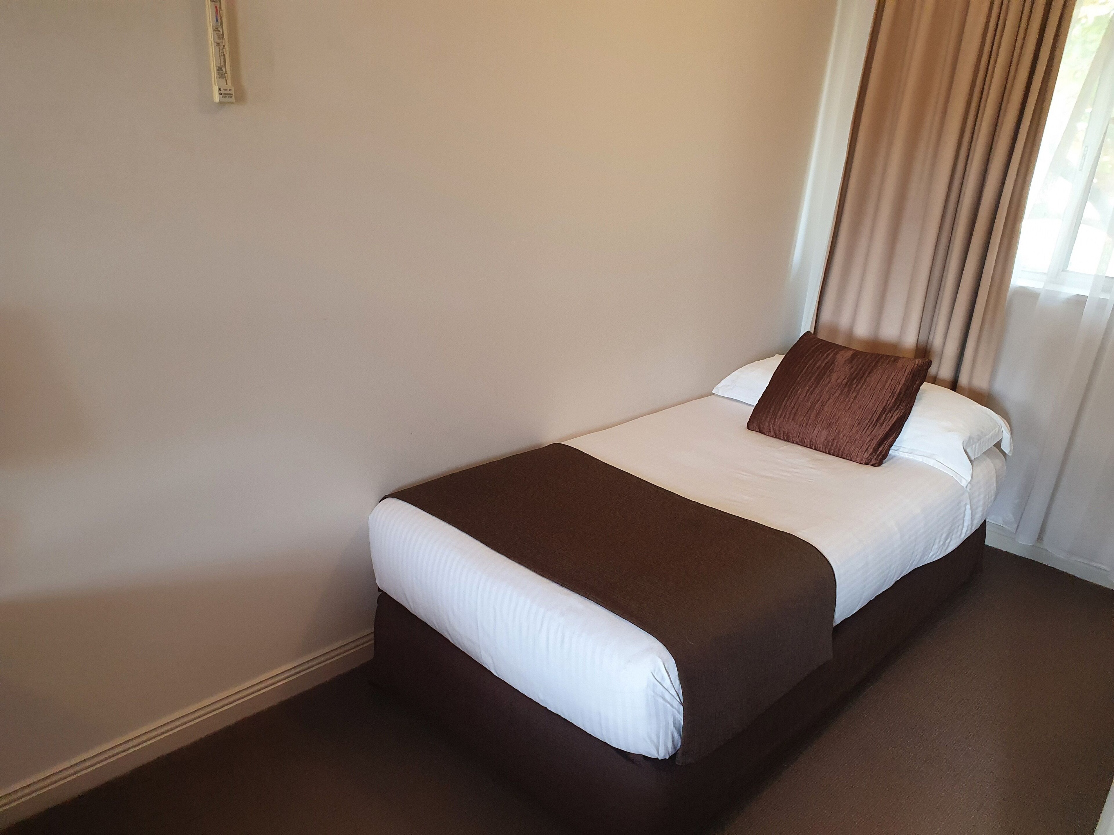 A neatly made bed with a brown headboard and white bedding in a hotel room.