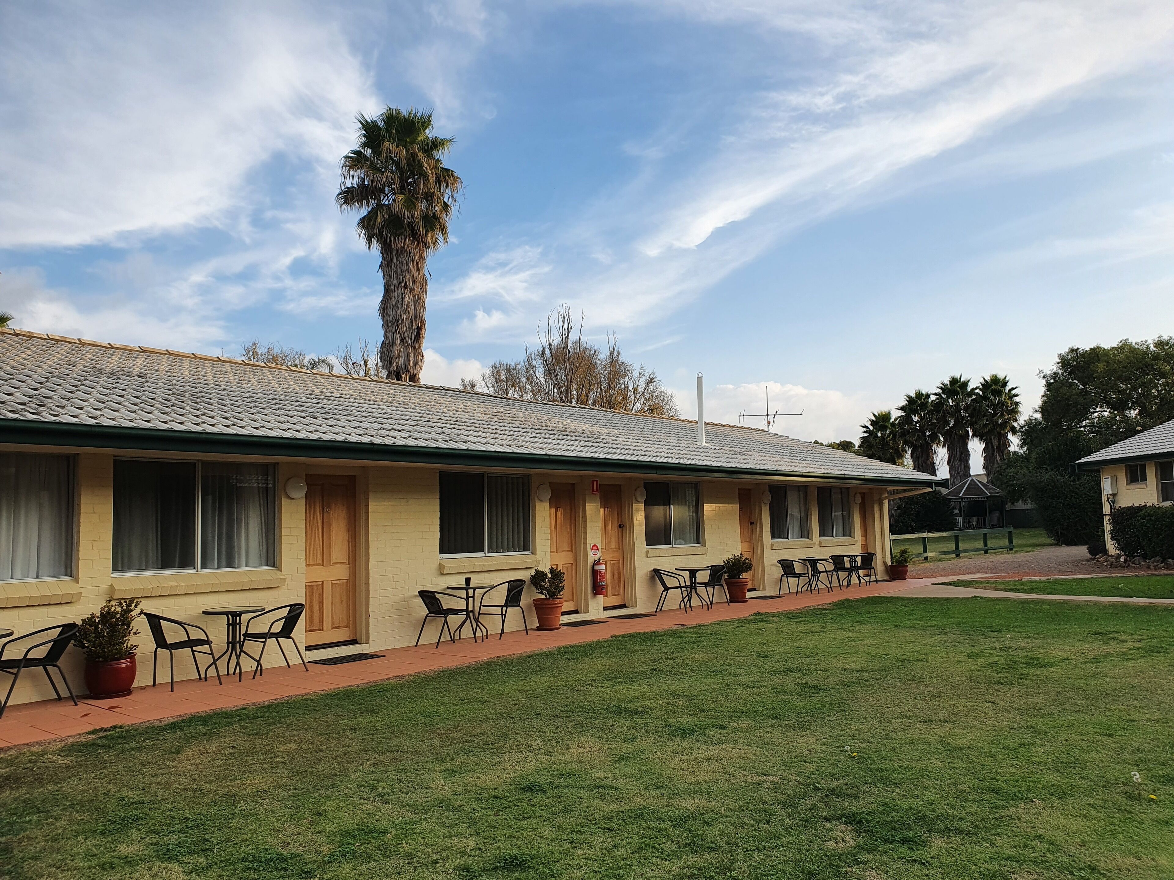 Een motel met pannendak, meerdere kamers, terras en gazon.