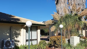 A house with a tiled roof, an air conditioning unit, and a garden with various plants and a tree.