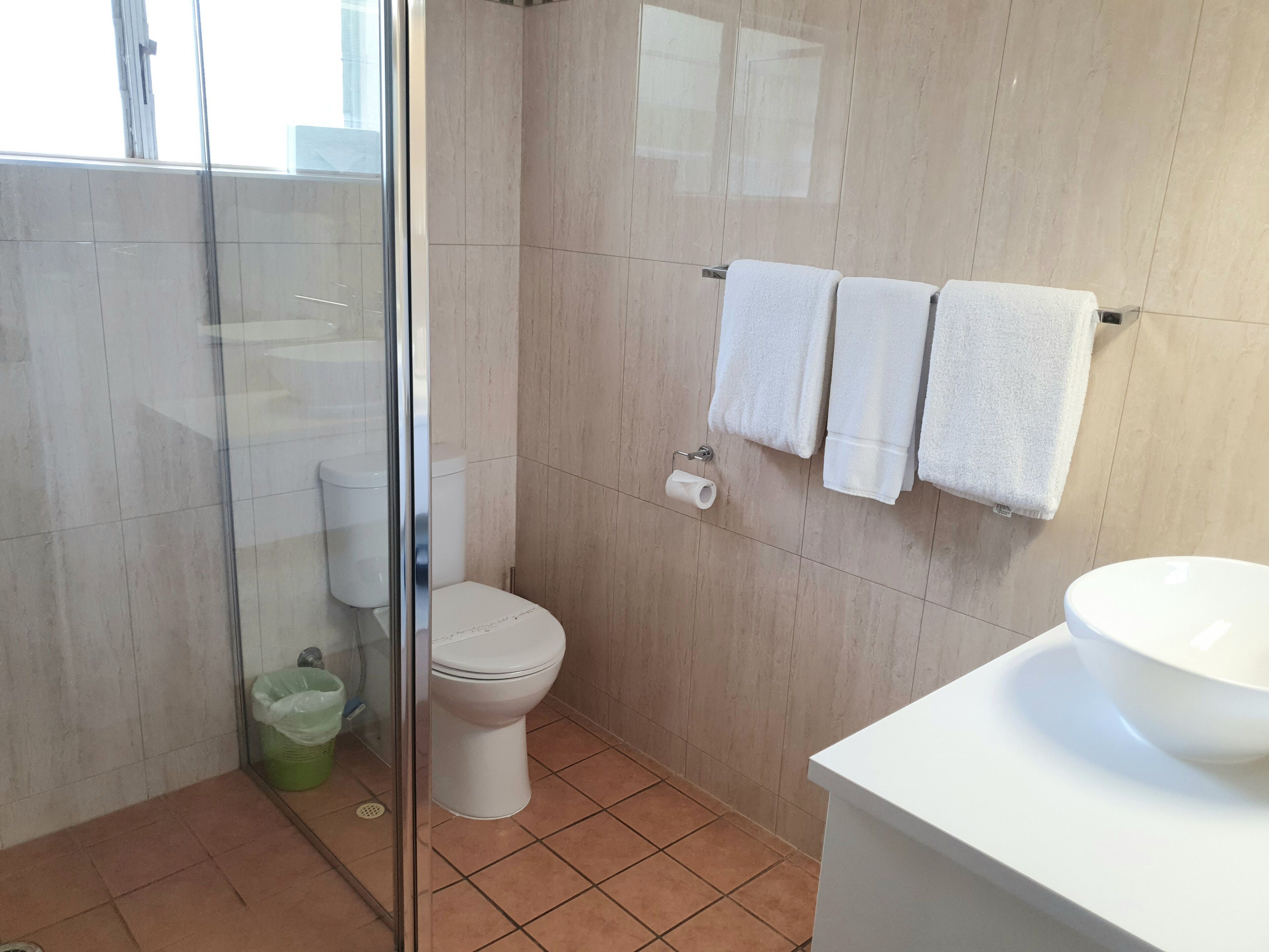 Un baño con cabina de ducha de vidrio, inodoro, lavabo y dos toallas colgadas en un perchero.