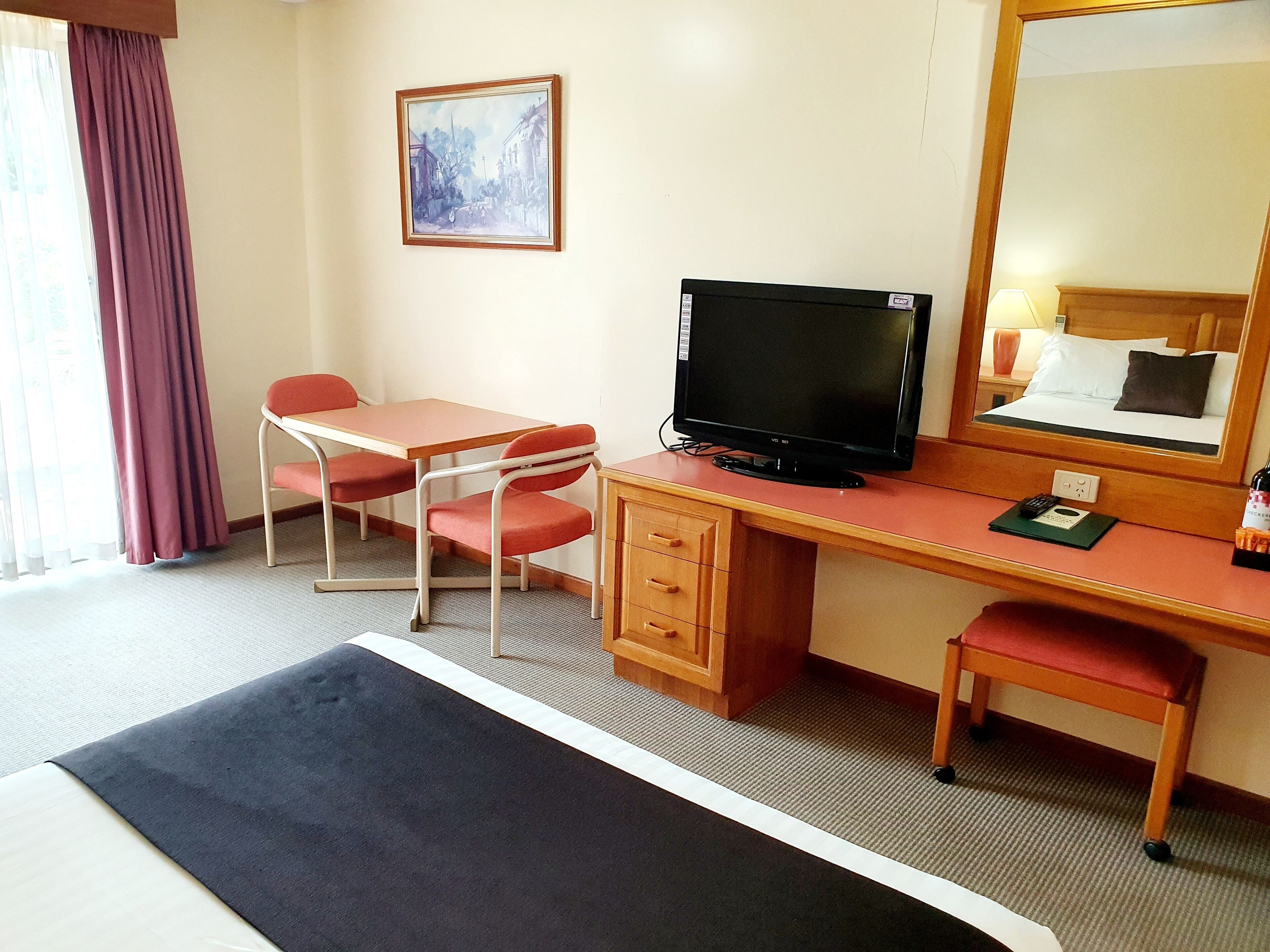 Une chambre d’hôtel avec un lit, un bureau avec un ordinateur, une chaise, une télévision et un tableau au mur.