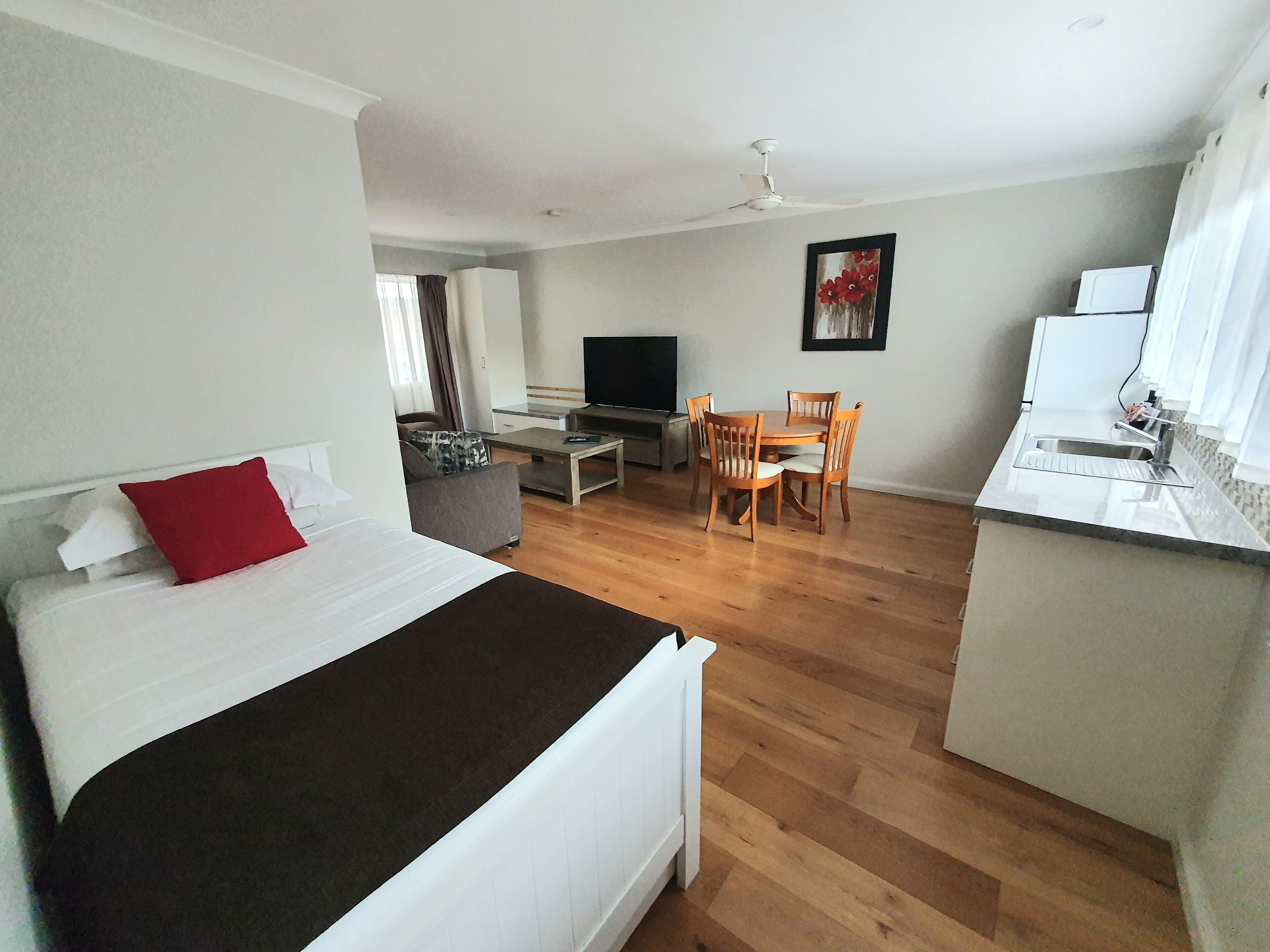 A hotel room with a bed, a desk, a TV, a dining table with chairs, and a kitchen area.
