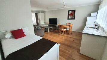 A hotel room with a bed, a desk, a TV, a dining table with chairs, and a kitchen area.