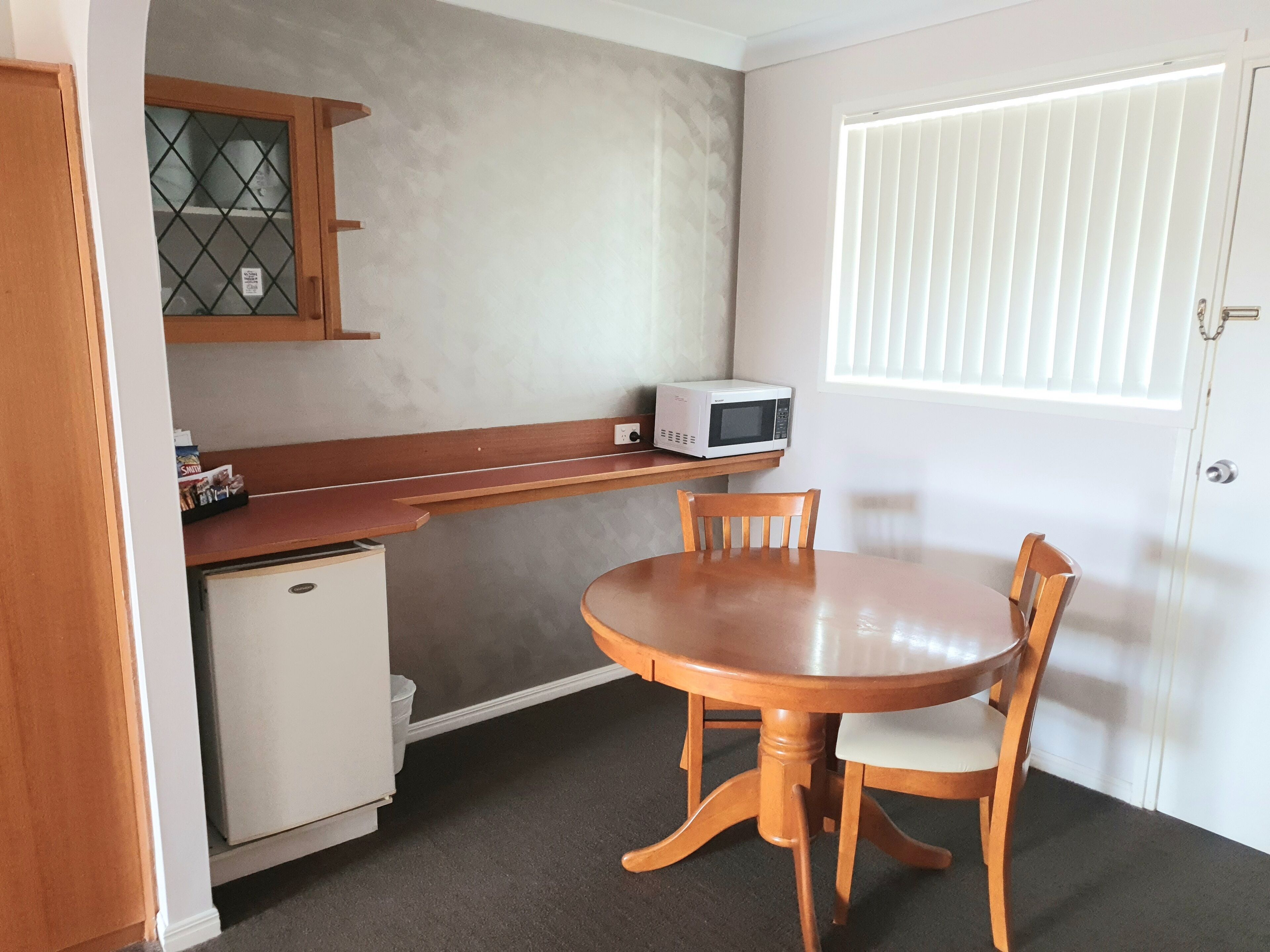 Una cocina compacta con microondas, un refrigerador pequeño y una mesa de madera con dos sillas.