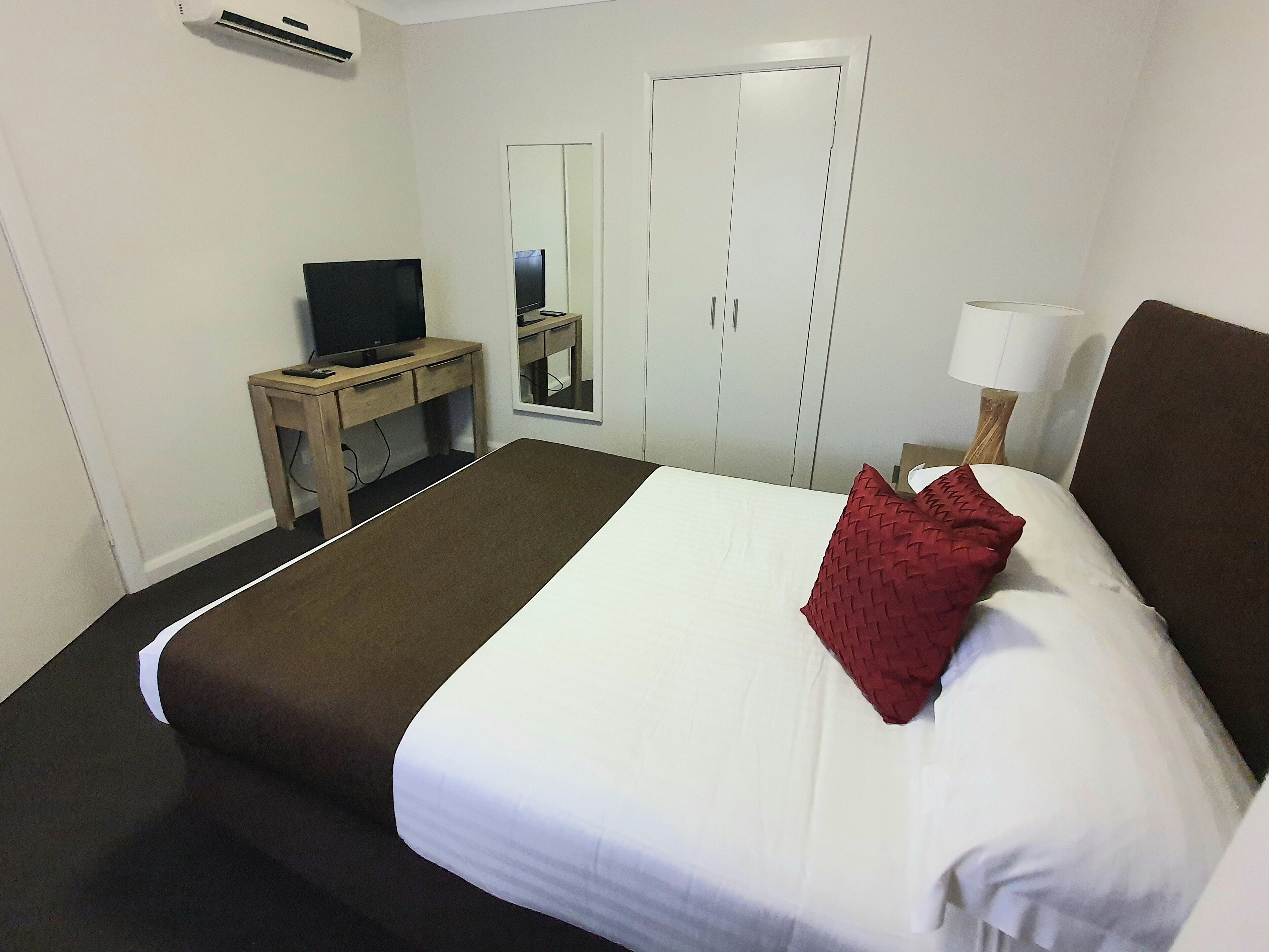 Una habitación de hotel con una cama, un escritorio con televisor, un espejo y una lámpara.