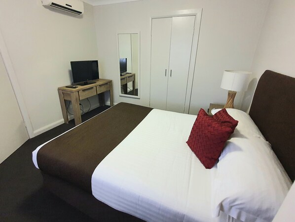 A hotel room with a bed, a desk with a TV, a mirror, and a lamp.