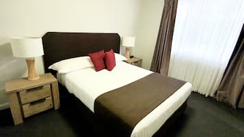 Ein Hotelzimmer mit einem großen Bett, zwei Nachttischen, einer Lampe auf jedem Tisch und einem Fenster mit Vorhängen.