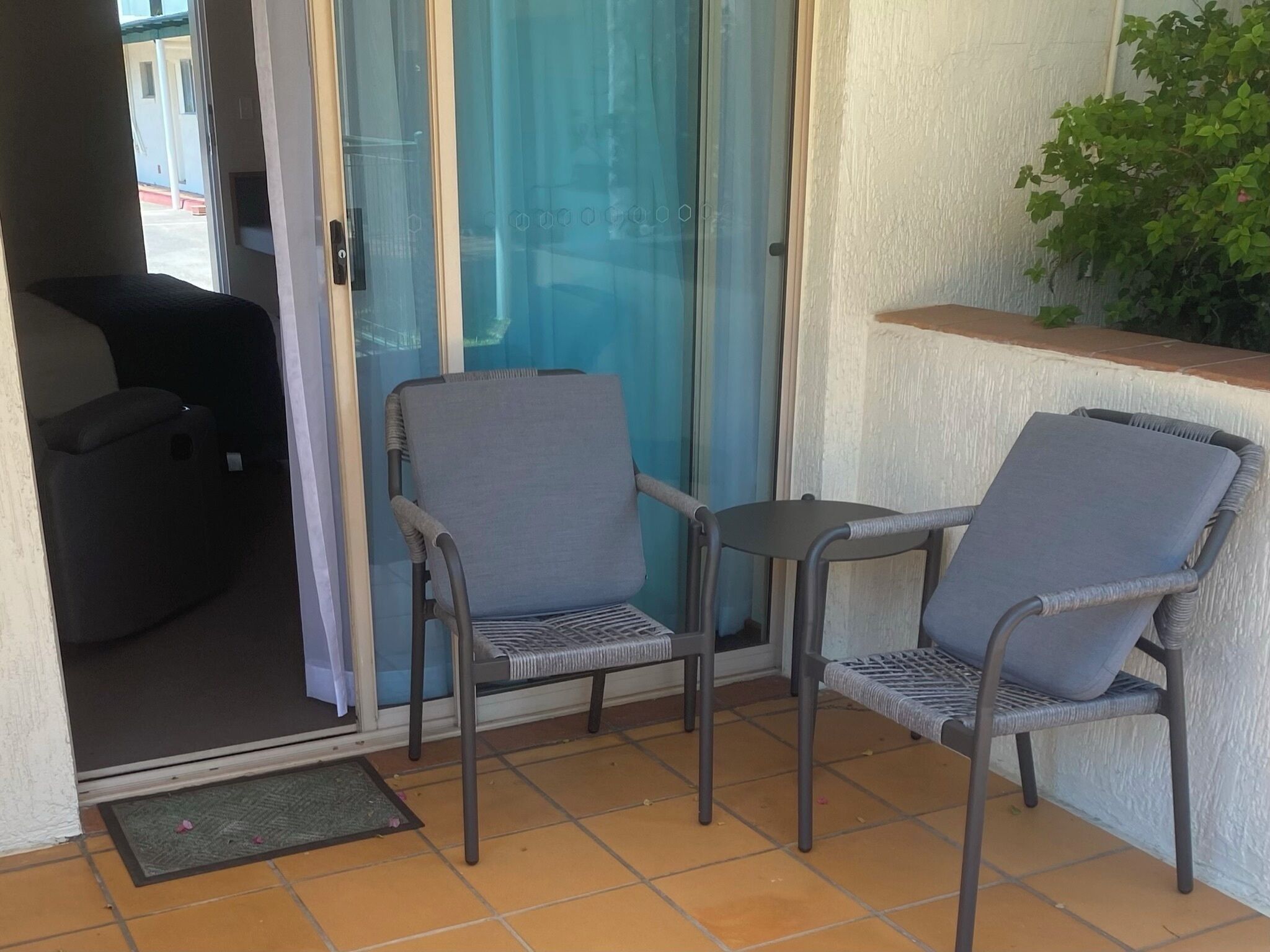 Un pequeño espacio al aire libre con dos sillas, una mesa, un ventanal corredero y una planta en maceta.