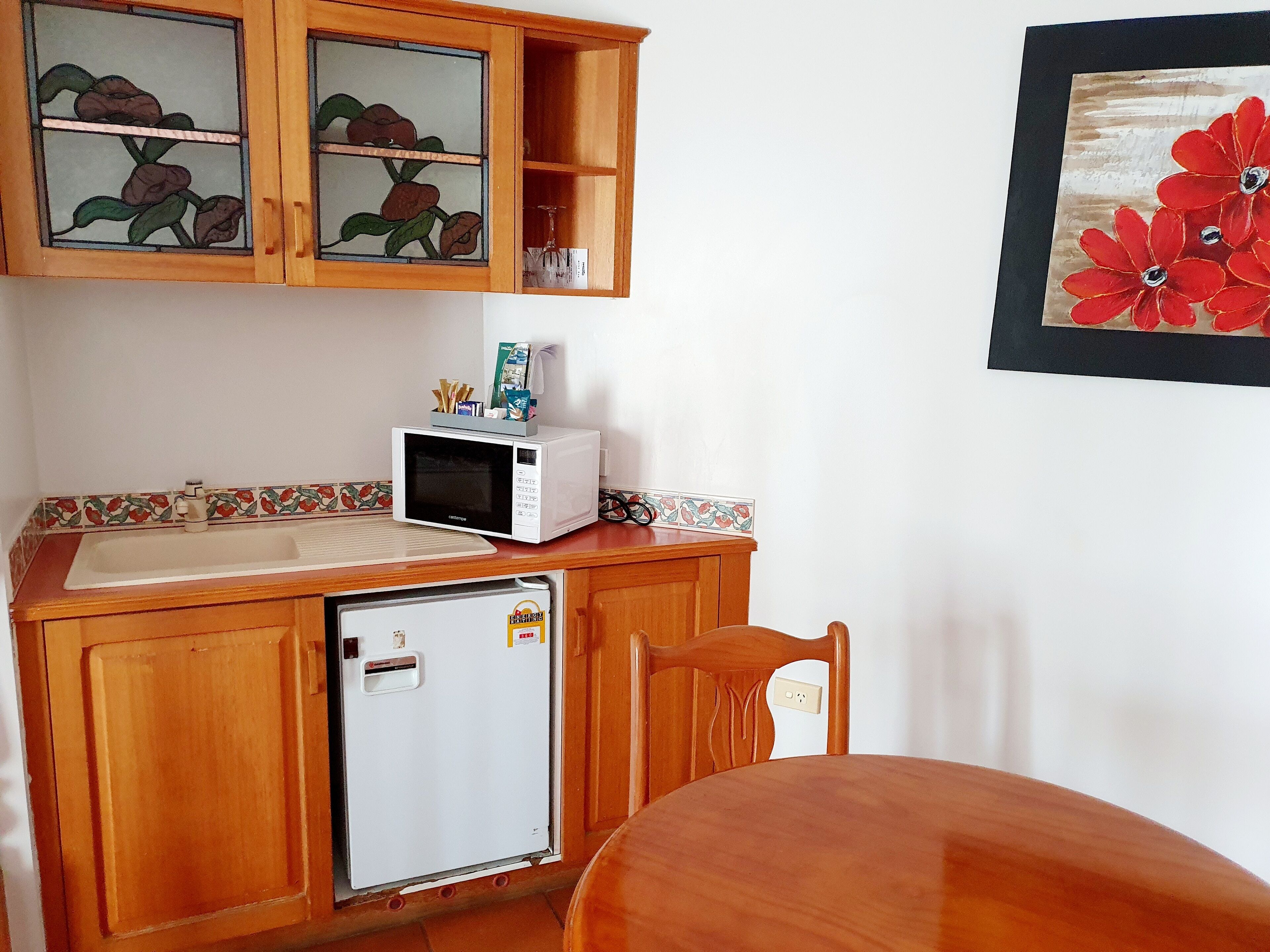 Een kleine keuken met een koelkast, magnetron en houten keukenkastjes.