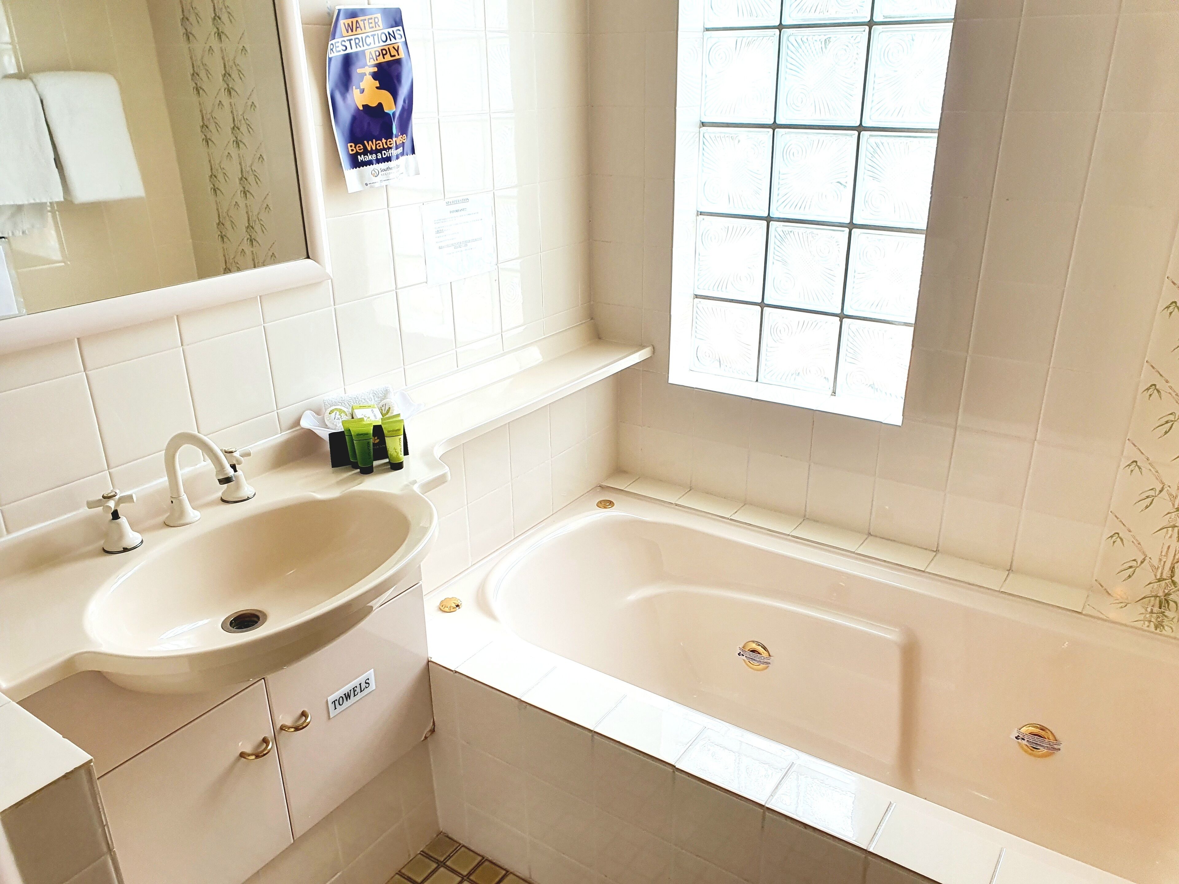 Un baño con lavamanos, dos grifos, bañera y ventana con diseño de cuadrícula.