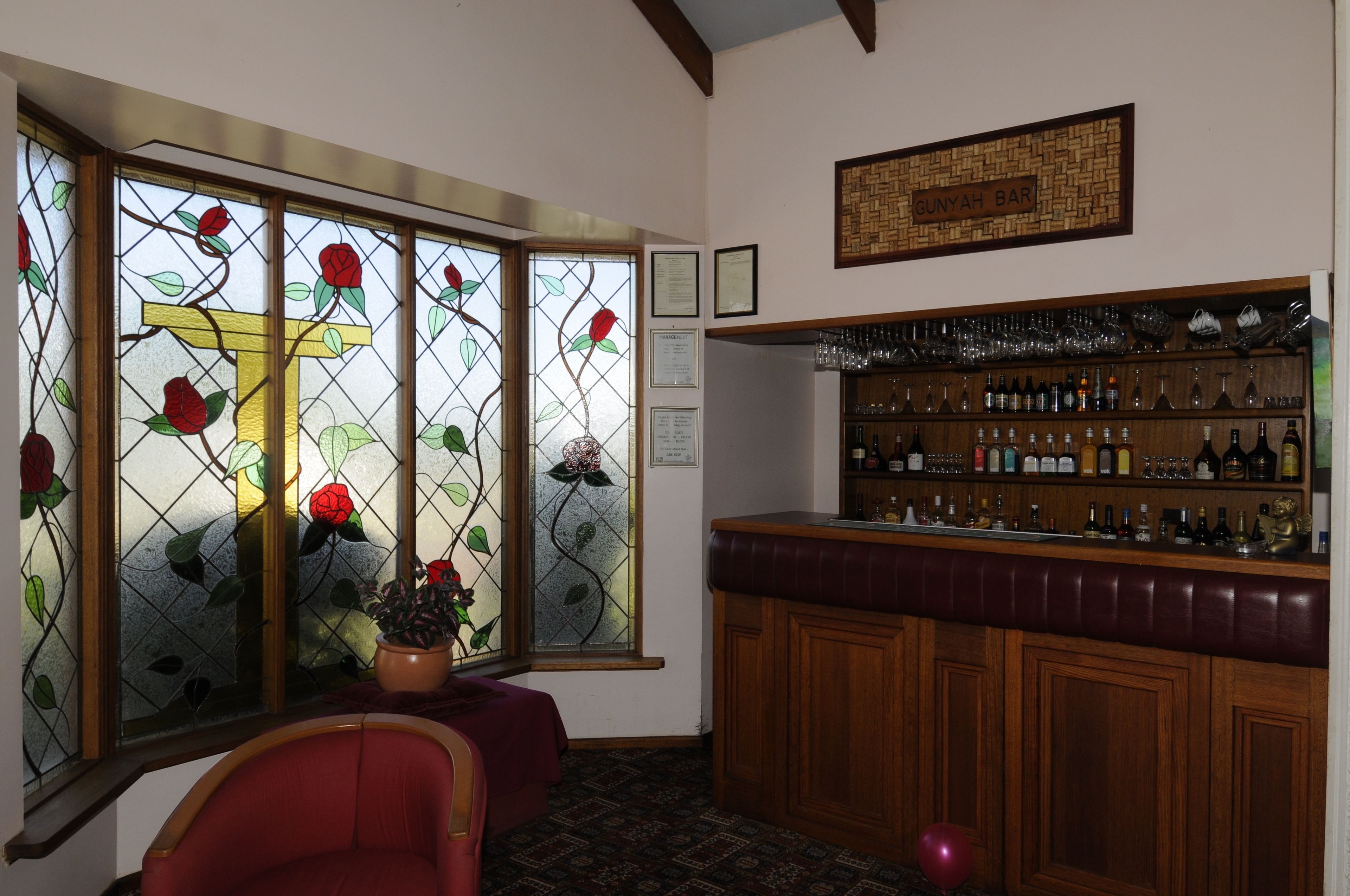 Eine Bar mit einer Holztheke, einem roten Stuhl und einem Rosenfenster aus Buntglas.