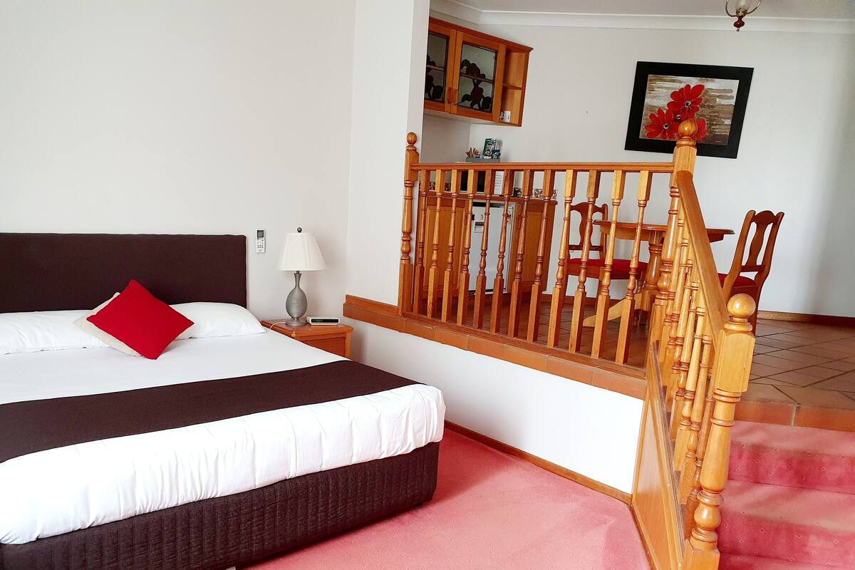 Une chambre d’hôtel avec un lit, une table de chevet, une lampe, un escalier en bois et un tableau au mur.
