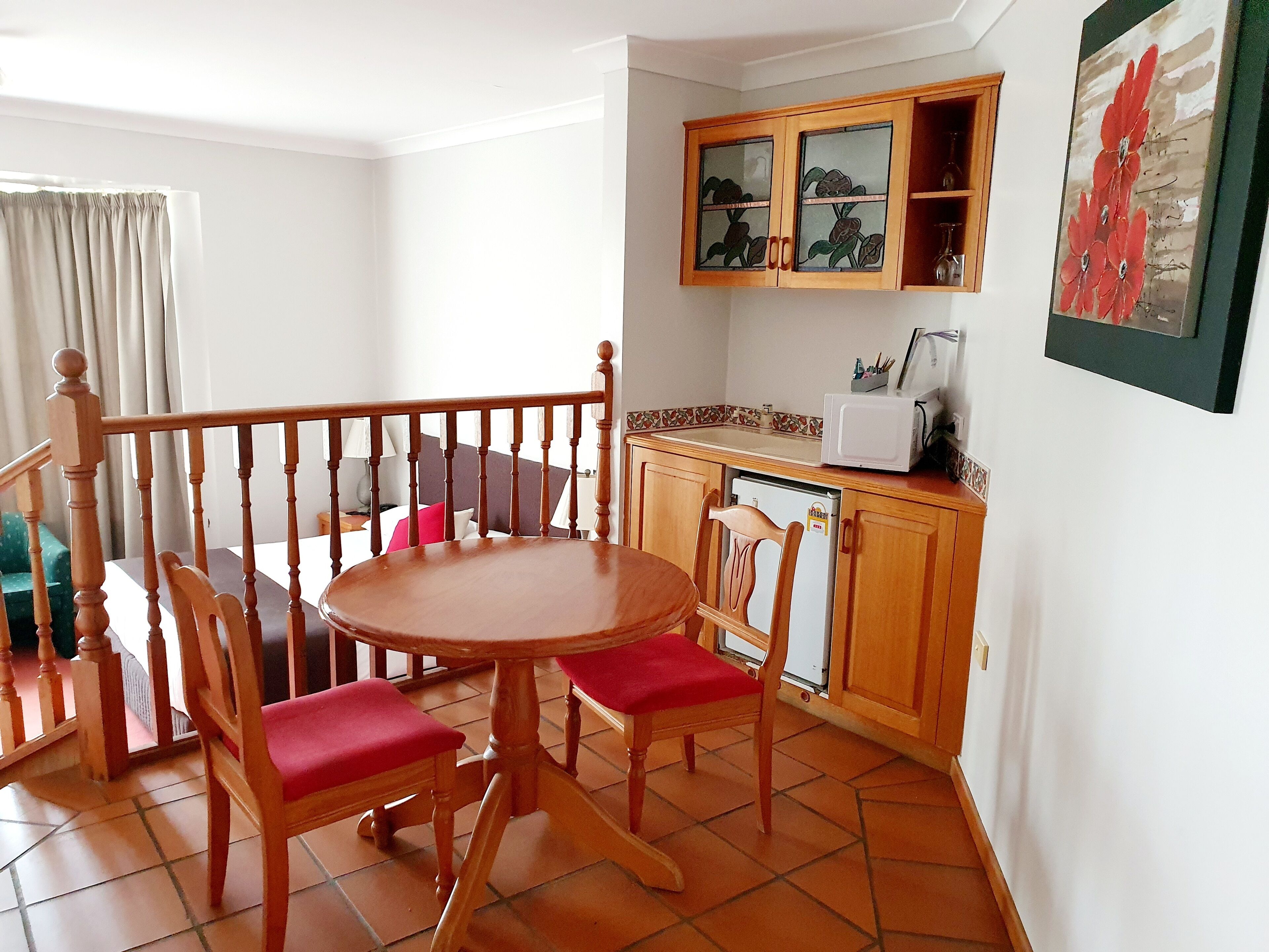 Un comedor con mesa y sillas de madera, una cocina con microondas y armarios, y un balcón con barandilla.
