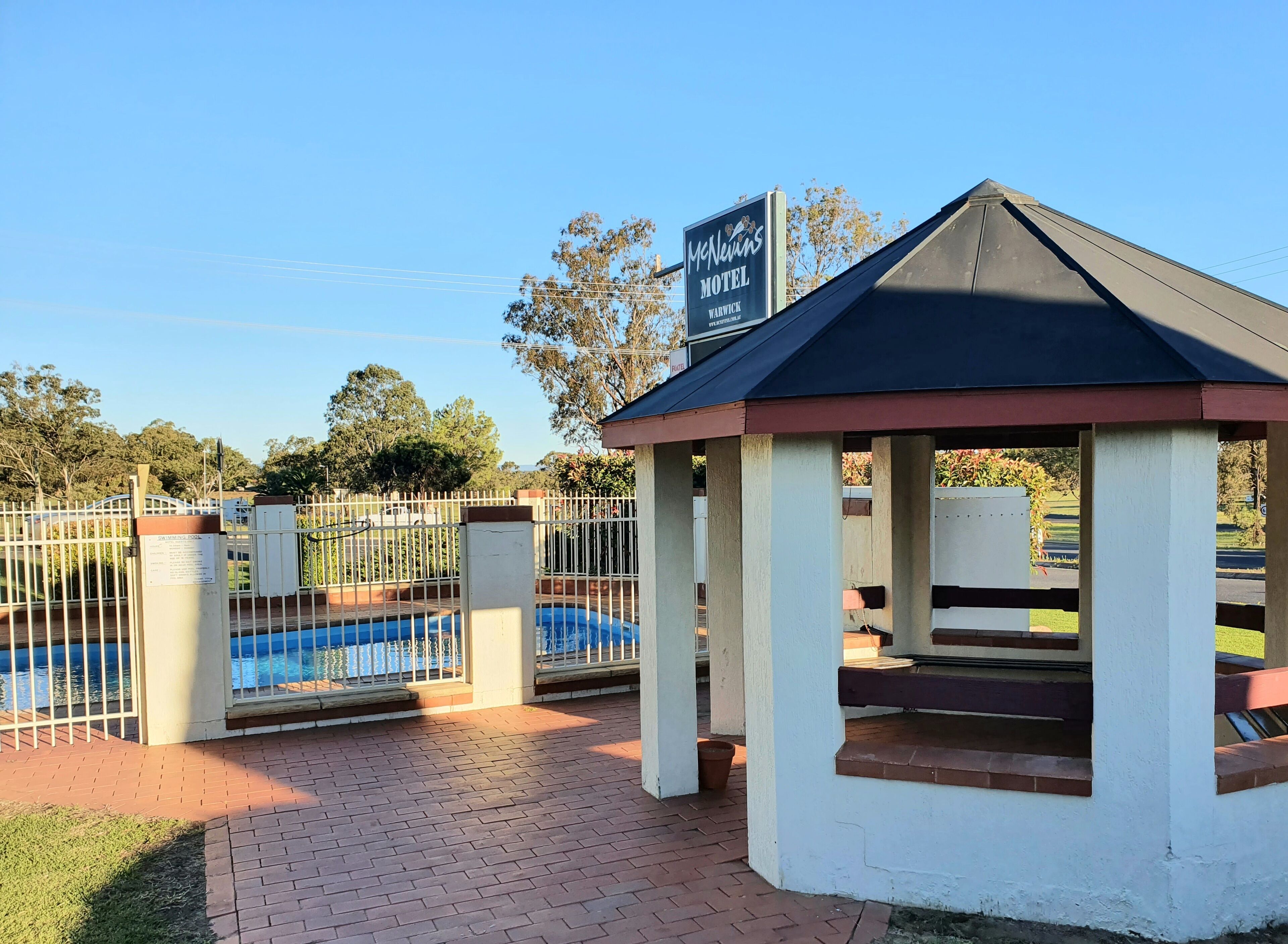 A motel with a swimming pool, a covered seating area, and a fenced entrance.