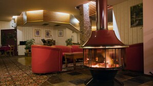 A cozy lounge area with a stone fireplace, red upholstered seating, and patterned carpet. - McNevin's Warwick Motel (Warwick)