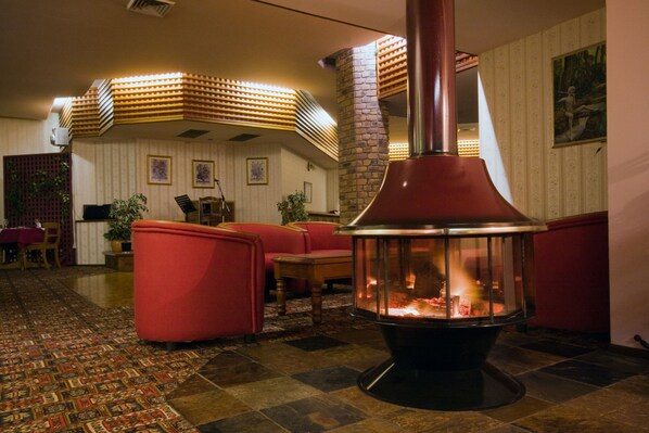 Eine gemütliche Lounge-Ecke mit Kamin aus Stein, roten Polstersesseln und einem gemusterten Teppich.