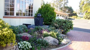 A building with a large window, a garden with various plants and flowers, and a paved walkway. - McNevin's Warwick Motel (Warwick)