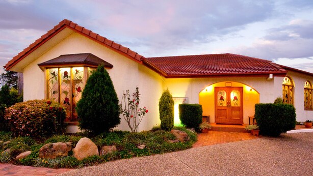 A two-story house with a red-tiled roof, a front porch, and a well-maintained garden with rocks and shrubs. - McNevin's Warwick Motel (Warwick)