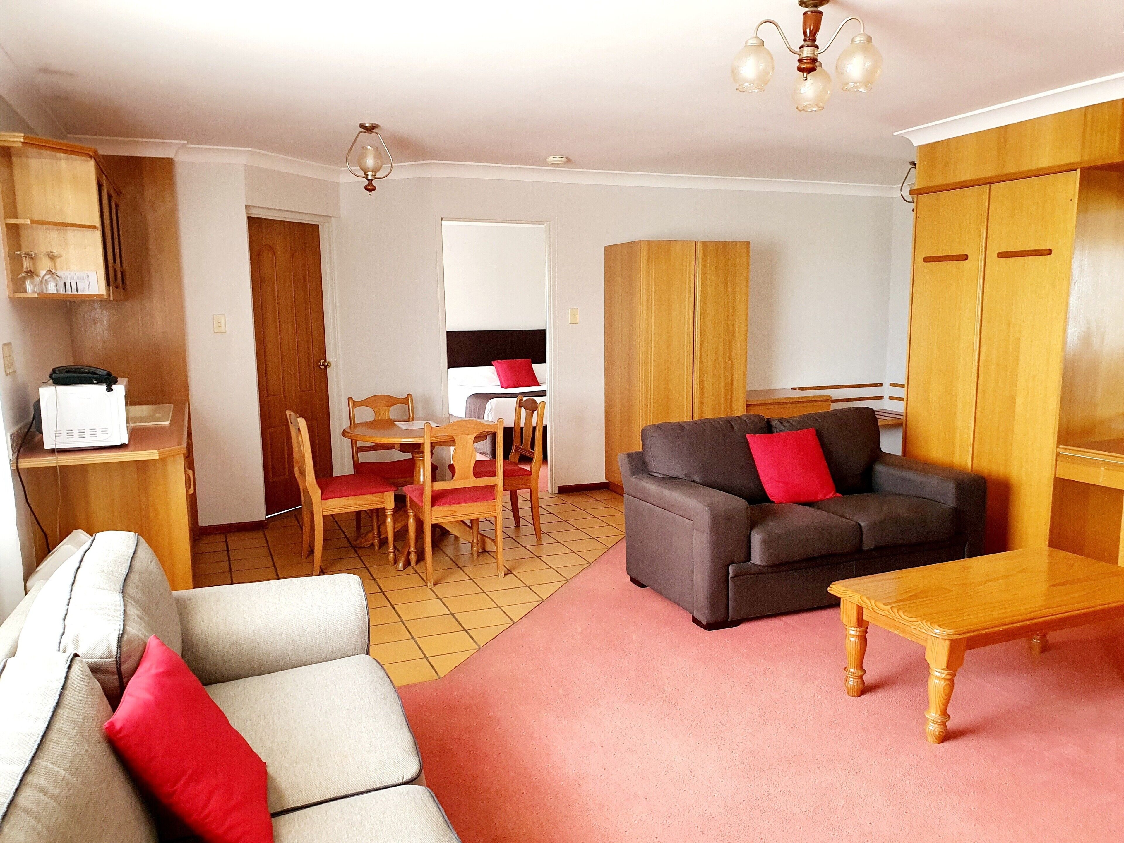 A living room with a sofa, a dining table with chairs, a kitchen area, and wooden cabinets.