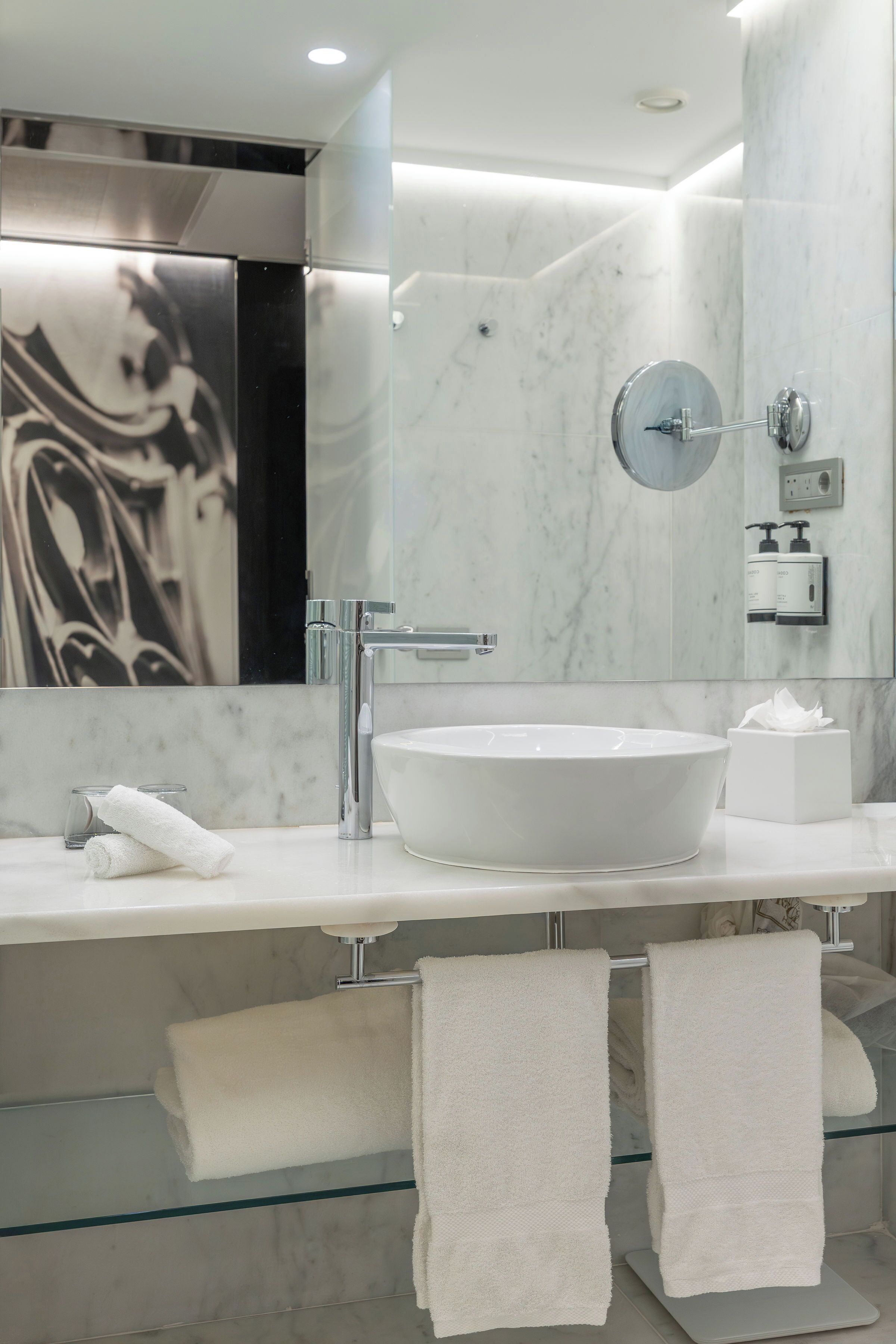 A modern bathroom with a large white sink, a mirror, and two towels on a glass shelf.