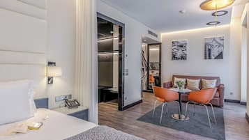 Une chambre d’hôtel comprenant un lit, un bureau avec un téléphone, un coin salon avec une table et des chaises, un canapé et des œuvres d’art accrochées aux murs.