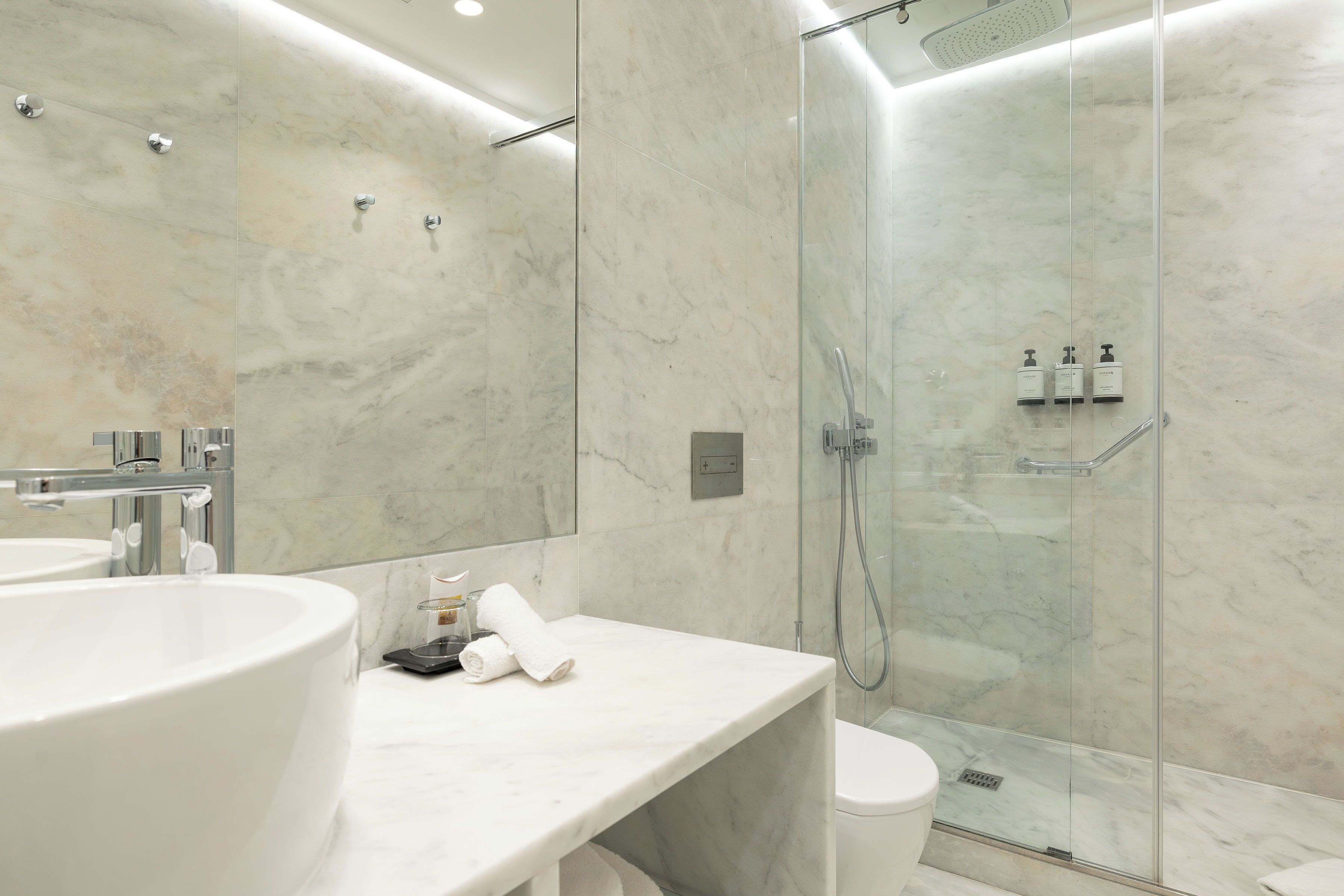 Un baño moderno con un lavamanos grande, cabina de ducha de vidrio y pared de mármol.
