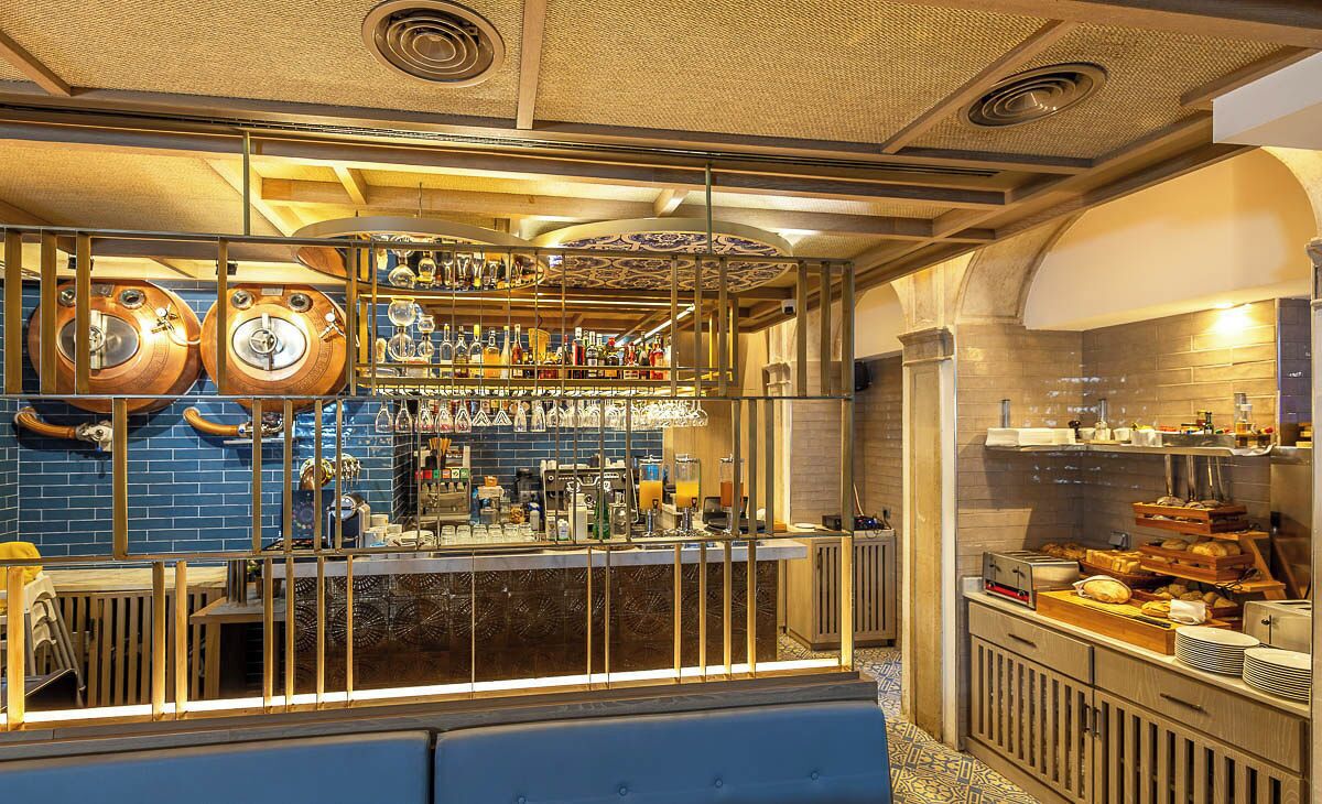 A bar area with wooden barrels, a variety of bottles, and a seating area with a blue bench.
