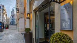 Entrada de hotel com placa indicando Hotel Santa Justa em Lisboa, um café, elevador e rua de calçada.