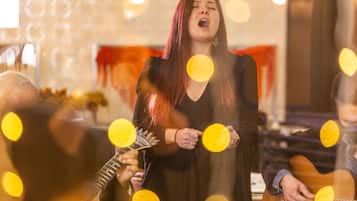 A person holding a guitar in a room with a patterned wall and a red object in the background.