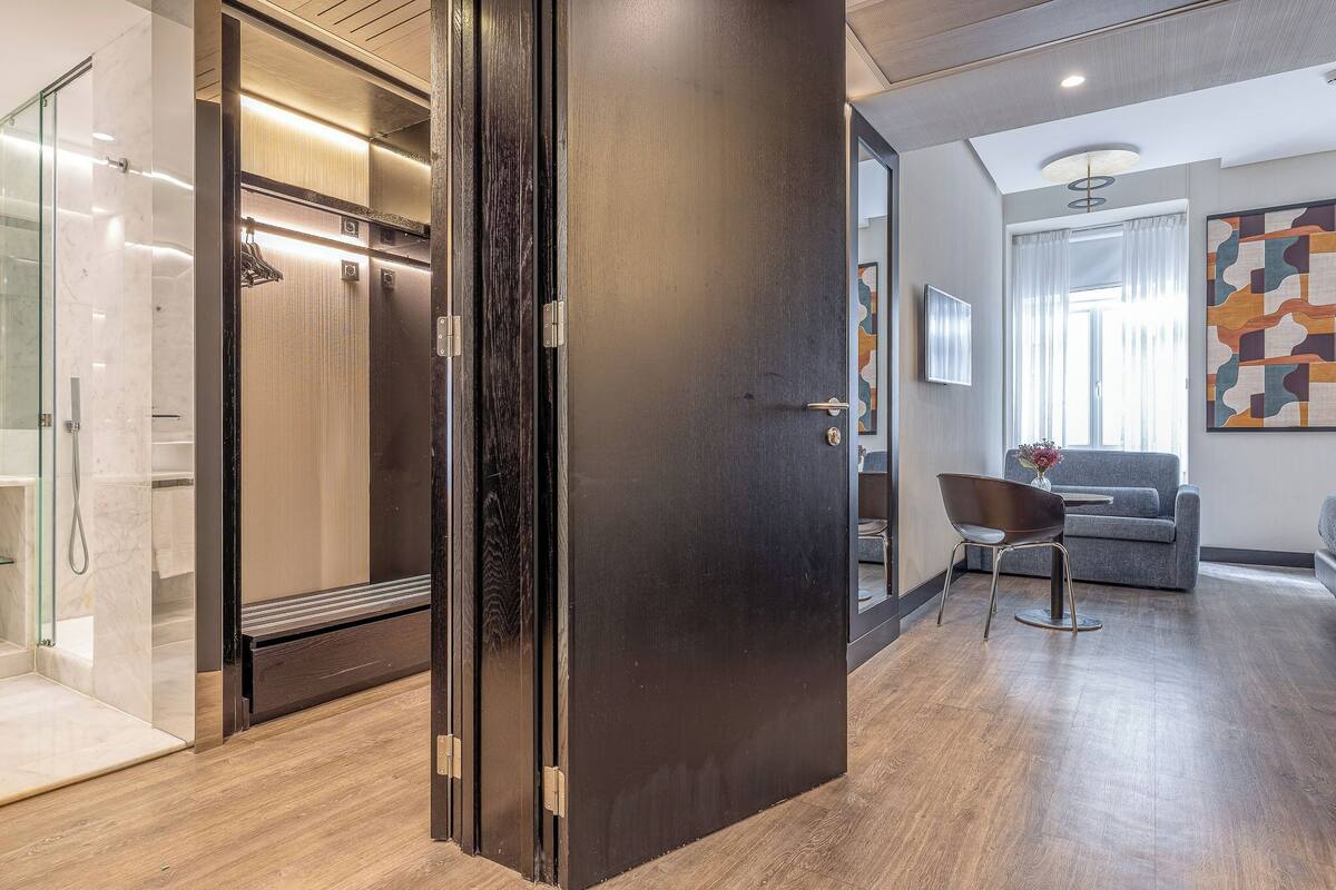 A modern interior with a wooden door, a glass shower enclosure, a grey sofa, and a wall-mounted TV.