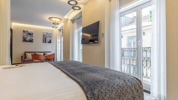 Una camera d'albergo con un letto grande, un divano, una televisione e un balcone con ringhiera.