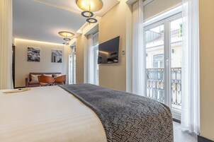 A hotel room with a large bed, a sofa, a TV, and a balcony with a railing.