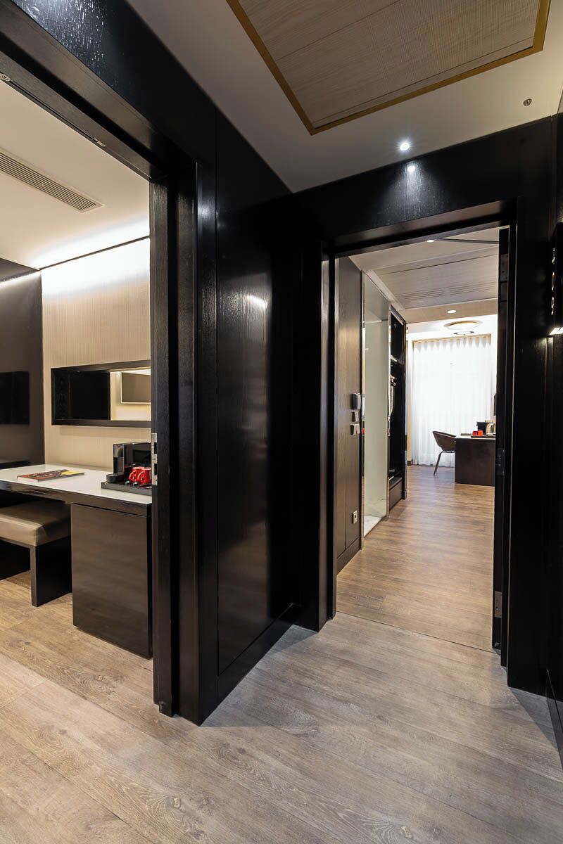 A modern hotel room with a wooden floor, a desk with a chair, a bed, and a large mirror.