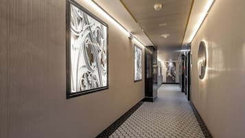 A corridor with patterned flooring, framed artwork on the walls, and a ceiling with recessed lighting.