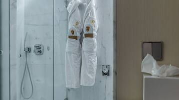 A modern bathroom with a glass-enclosed shower, white marble walls, and a towel rack with white robes.